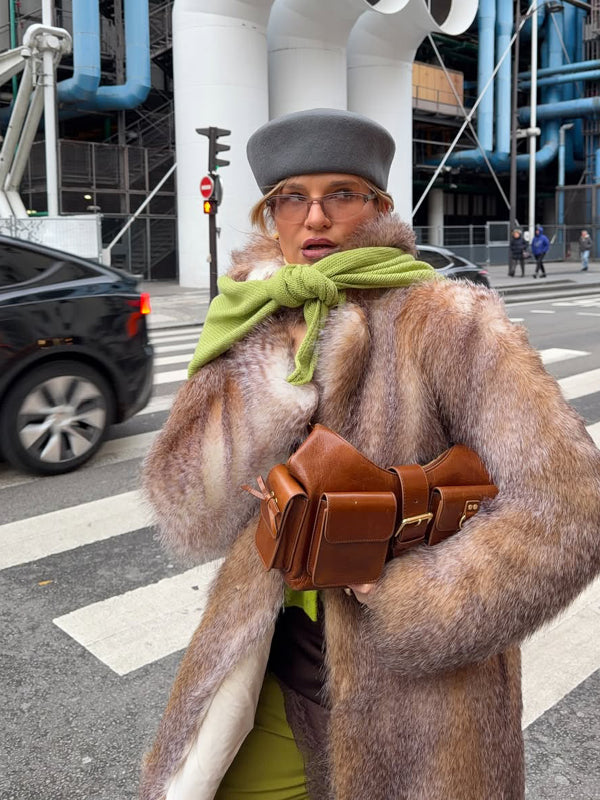 Person wearing a fur coat and green scarf on a city street