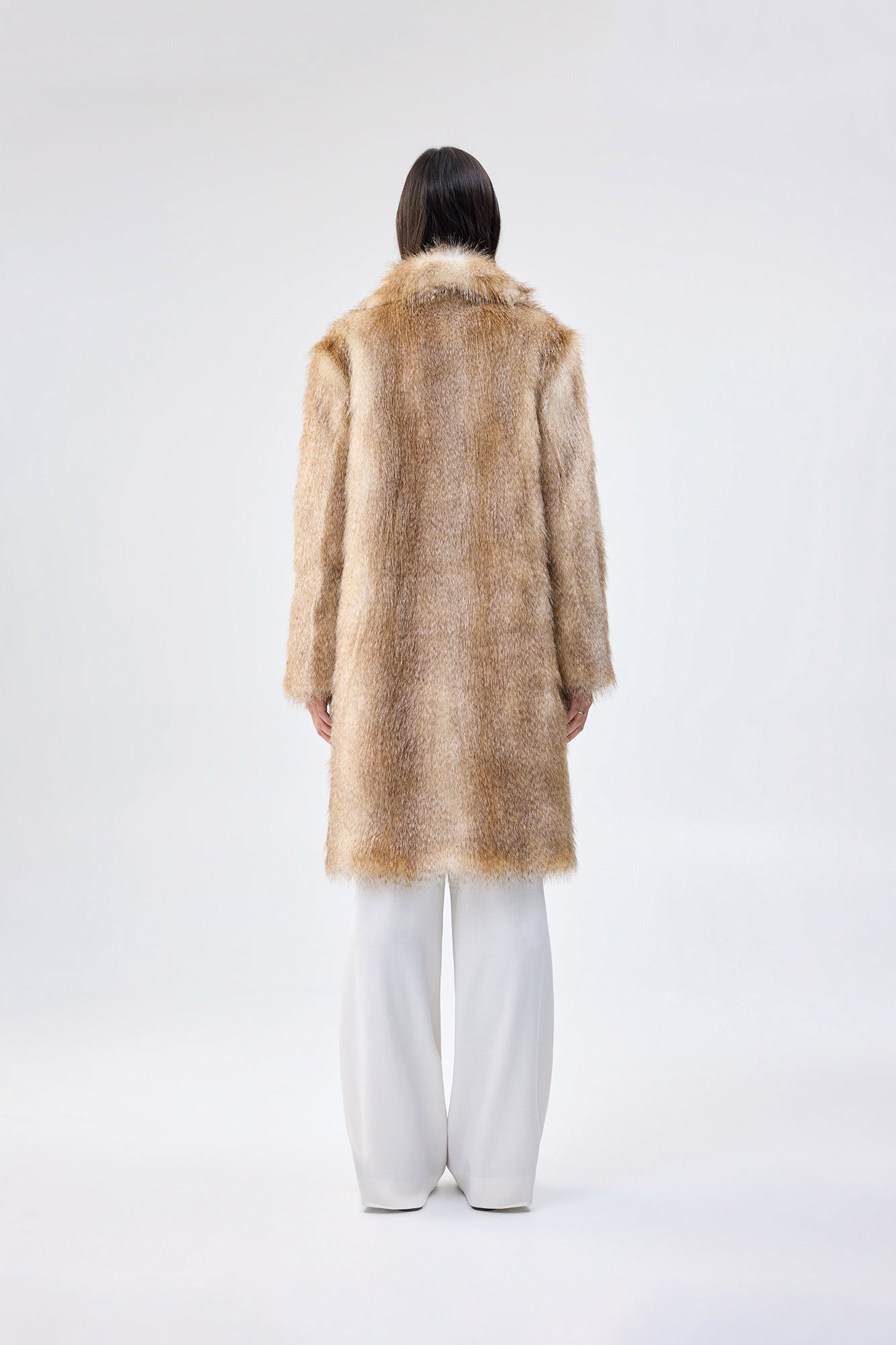 back view of a person wearing a faux fur coat and white pants on a white background