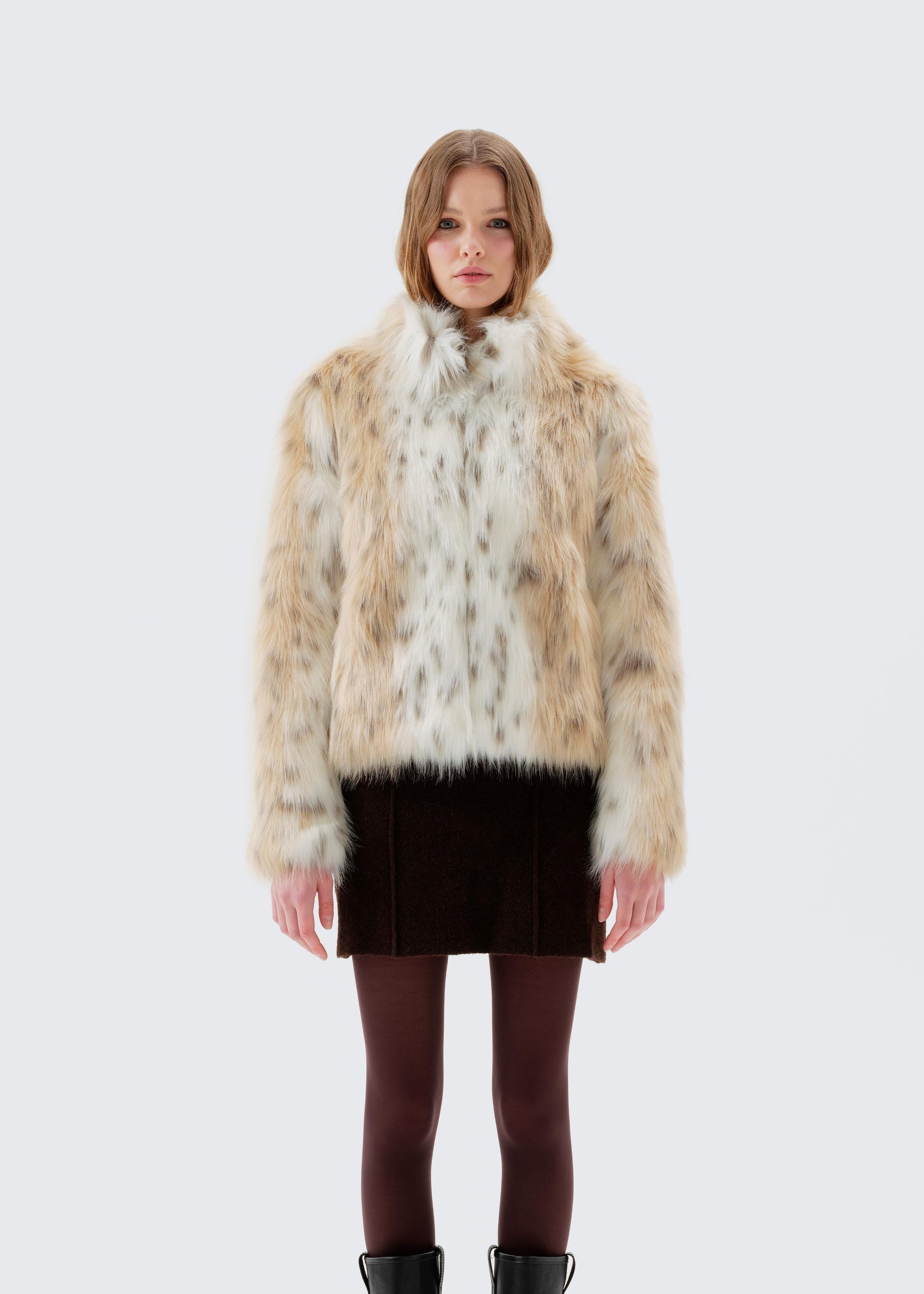 Woman wearing a faux fur vest, skirt, and boots on a white background